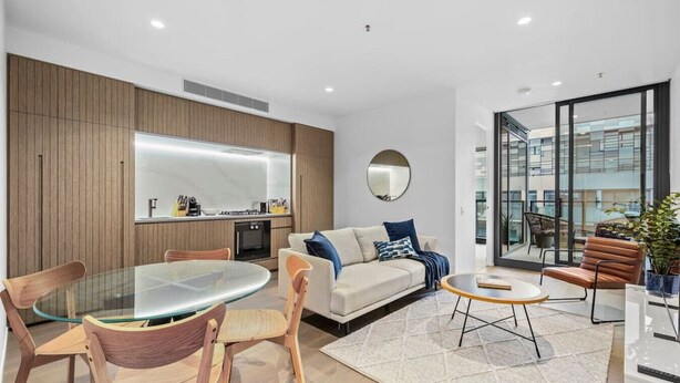 A modern living room with a glass dining table, wooden chairs, a sofa with blue cushions, and a coffee table. - The Park House City Retreat on the Yarra River (Abbotsford)