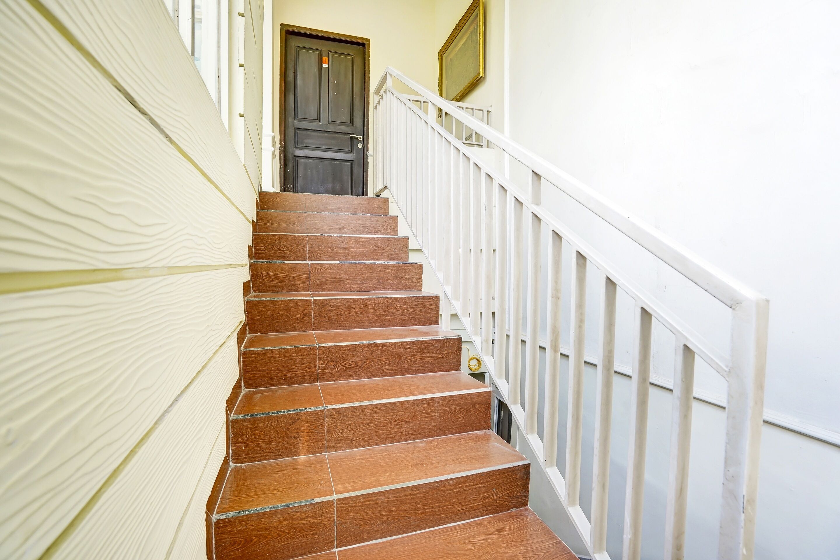 Una escalera con escalones de madera y barandillas blancas, que conduce a una puerta oscura.