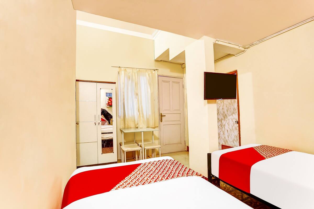Quarto de hotel com duas camas, televisão, guarda-roupa e secretária com cadeiras.