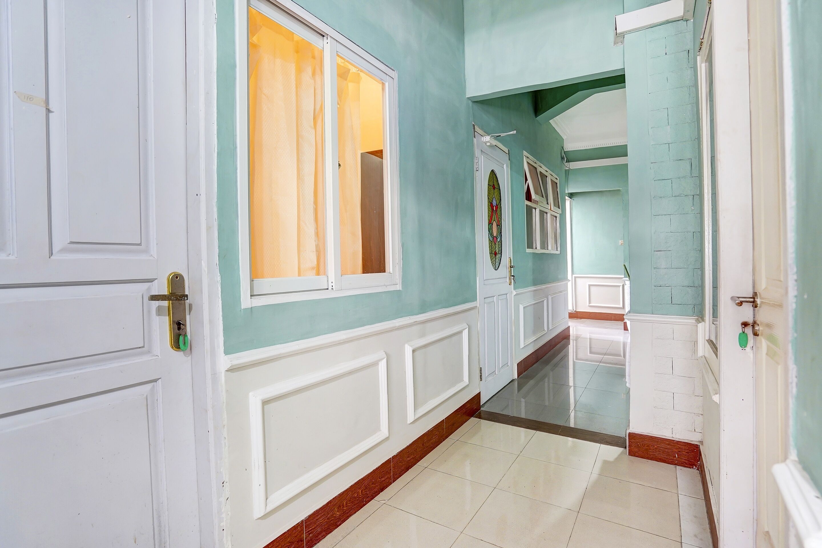 Un pasillo con puertas blancas, suelo de baldosas y pared verde.
