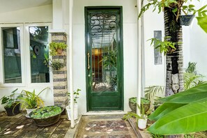Una puerta verde con reja de metal, plantas en macetas y un acceso con suelo de piedra.
