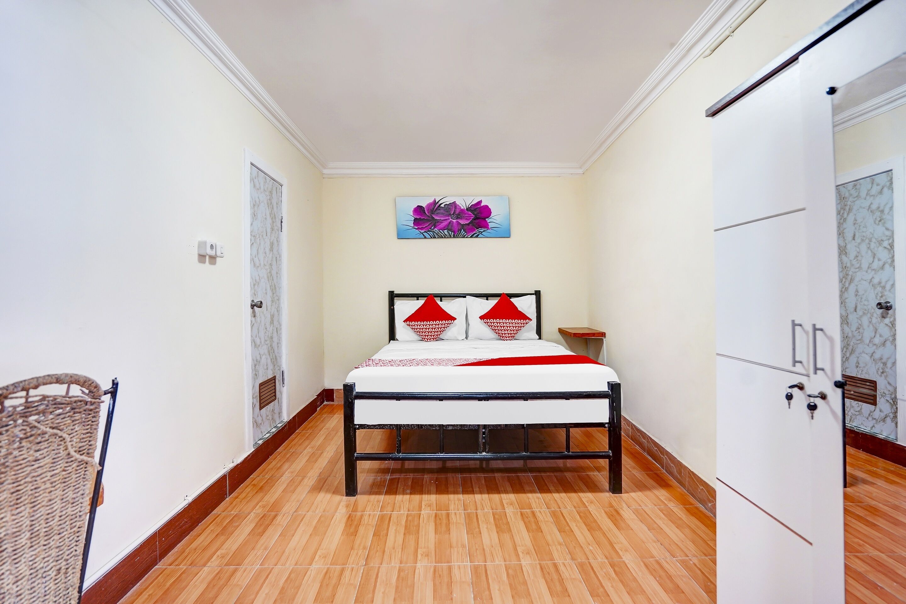 A bedroom with a bed, a painting, a door, and a wardrobe.