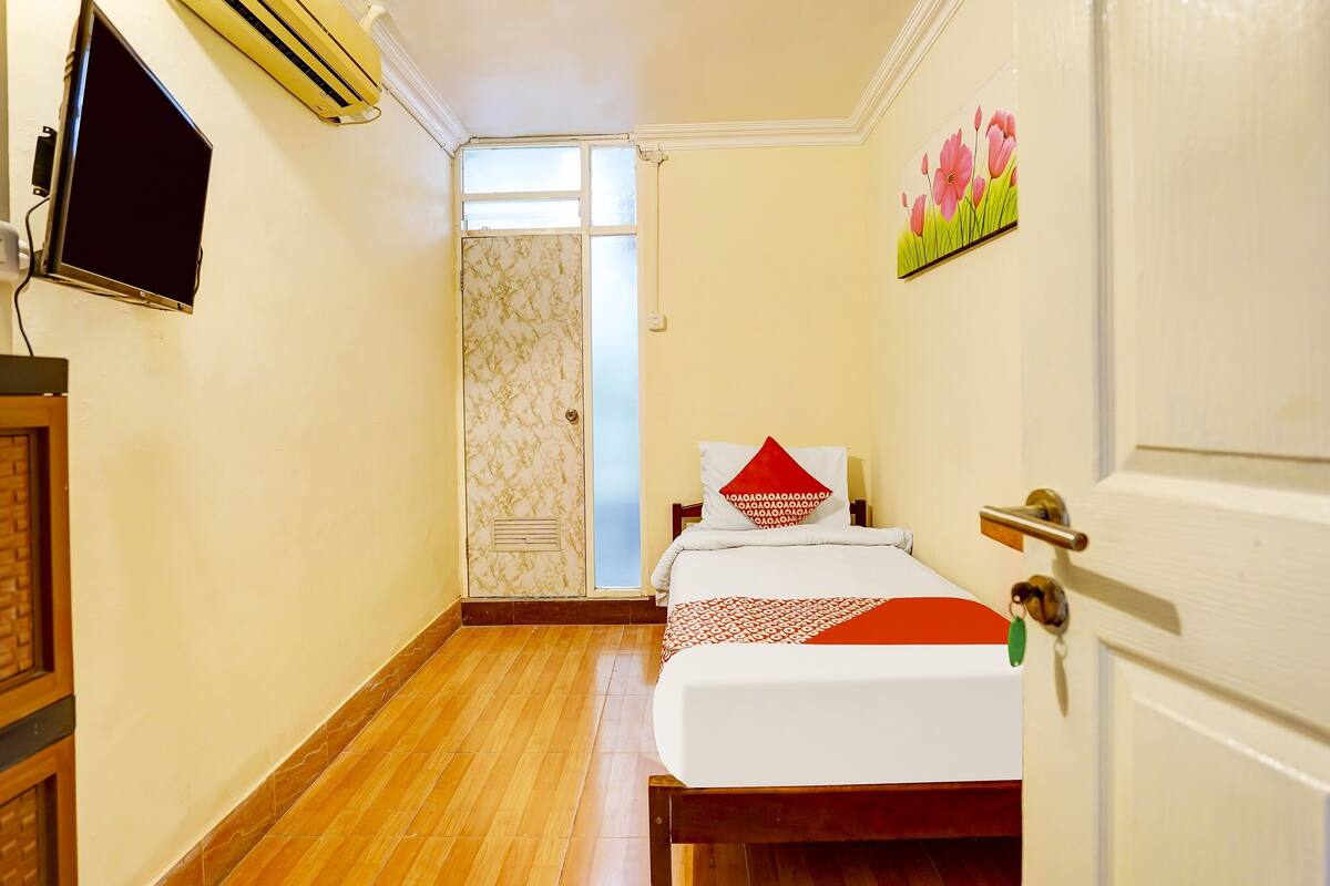 Quarto de hotel com cama, televisão, ar condicionado e porta com puxador.