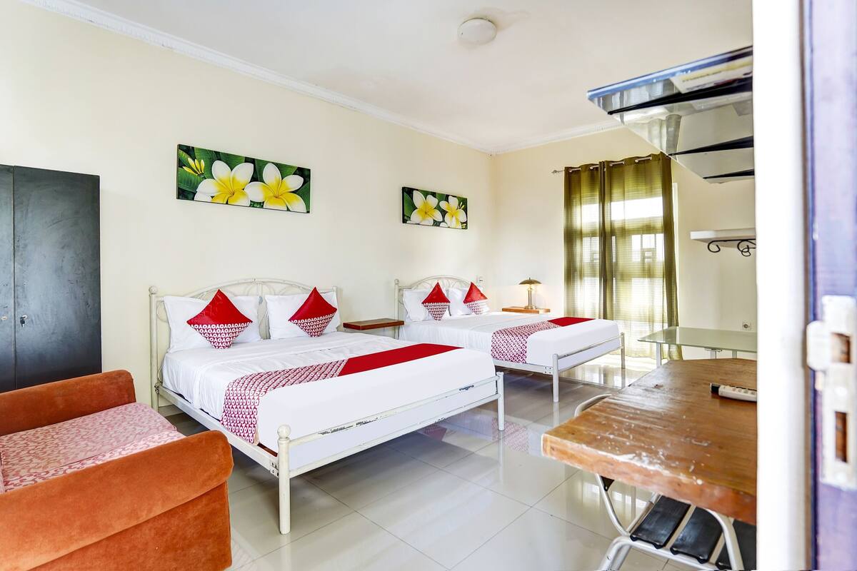 Quarto de hotel com duas camas, um sofá, uma mesa de jantar e obras de arte nas paredes.