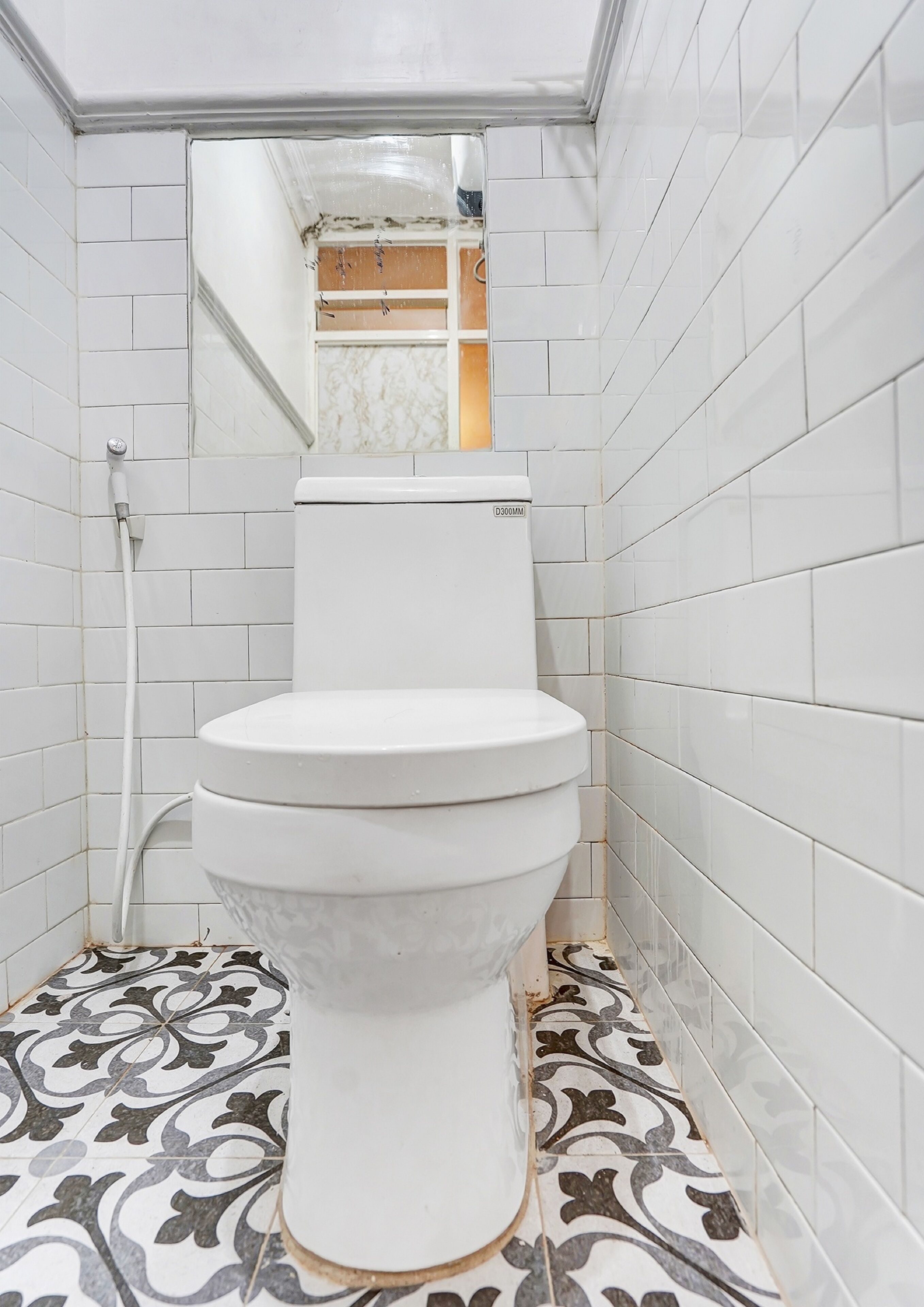 Een kleine, smalle badkamer met witte betegelde muren en een vloer met patroon.