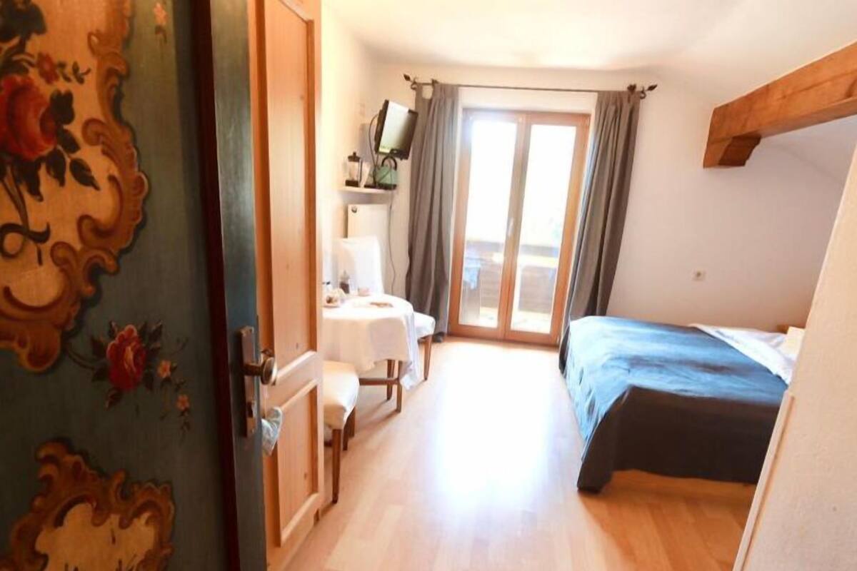 Una habitación con cama, escritorio con silla, ventana con cortinas y puerta con diseño floral.