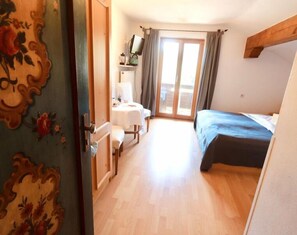 Una habitación con cama, escritorio con silla, ventana con cortinas y puerta con diseño floral.