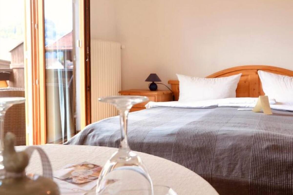 Habitación de hotel con cama, mesita de noche, lámpara y vista a través de un ventanal.