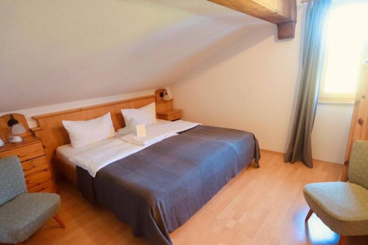 Un dormitorio con cama de madera, mesita de noche, una silla y ventana con cortinas.