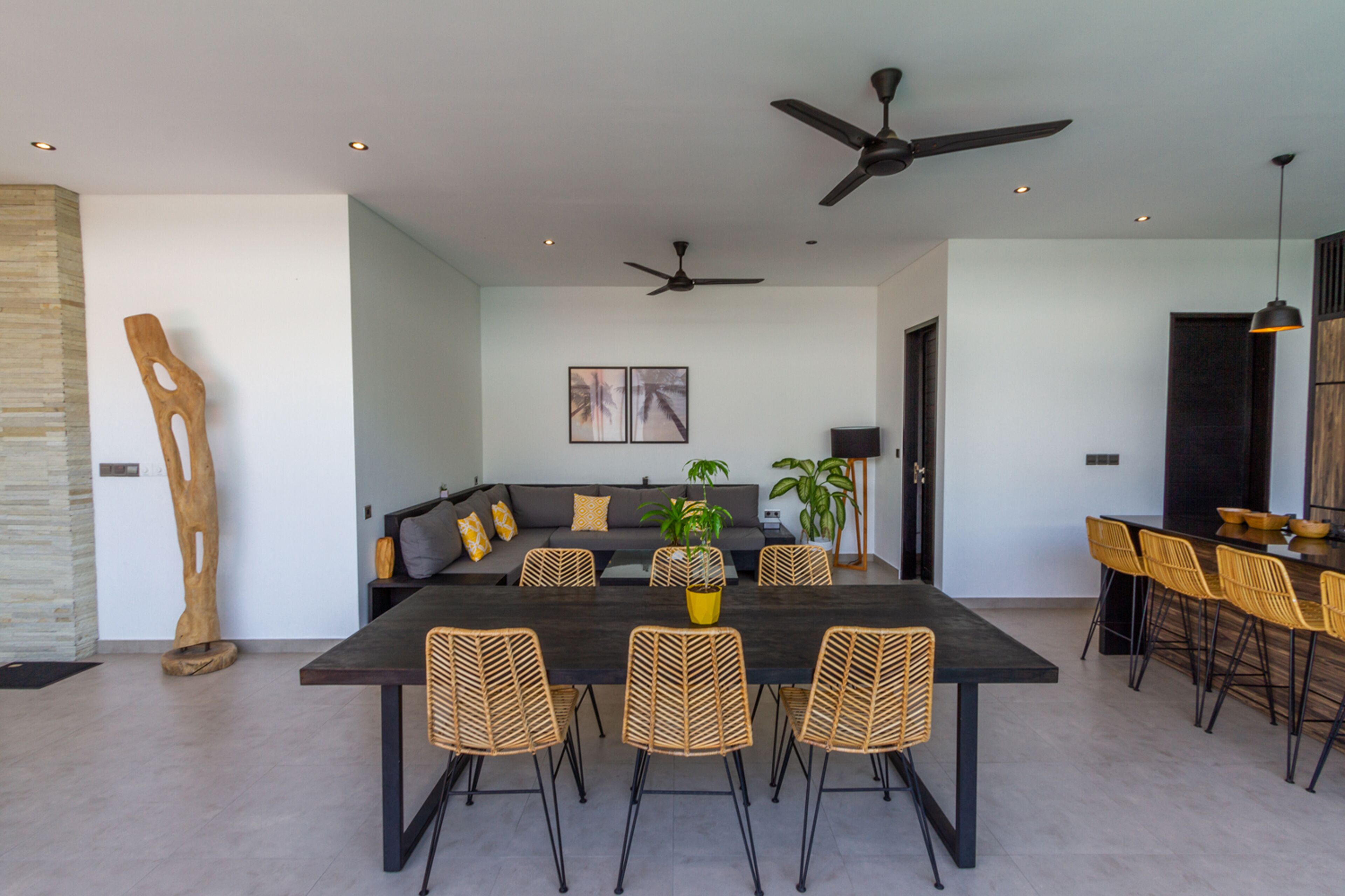 A modern dining area with a dark wooden table, wicker chairs, and a ceiling fan.