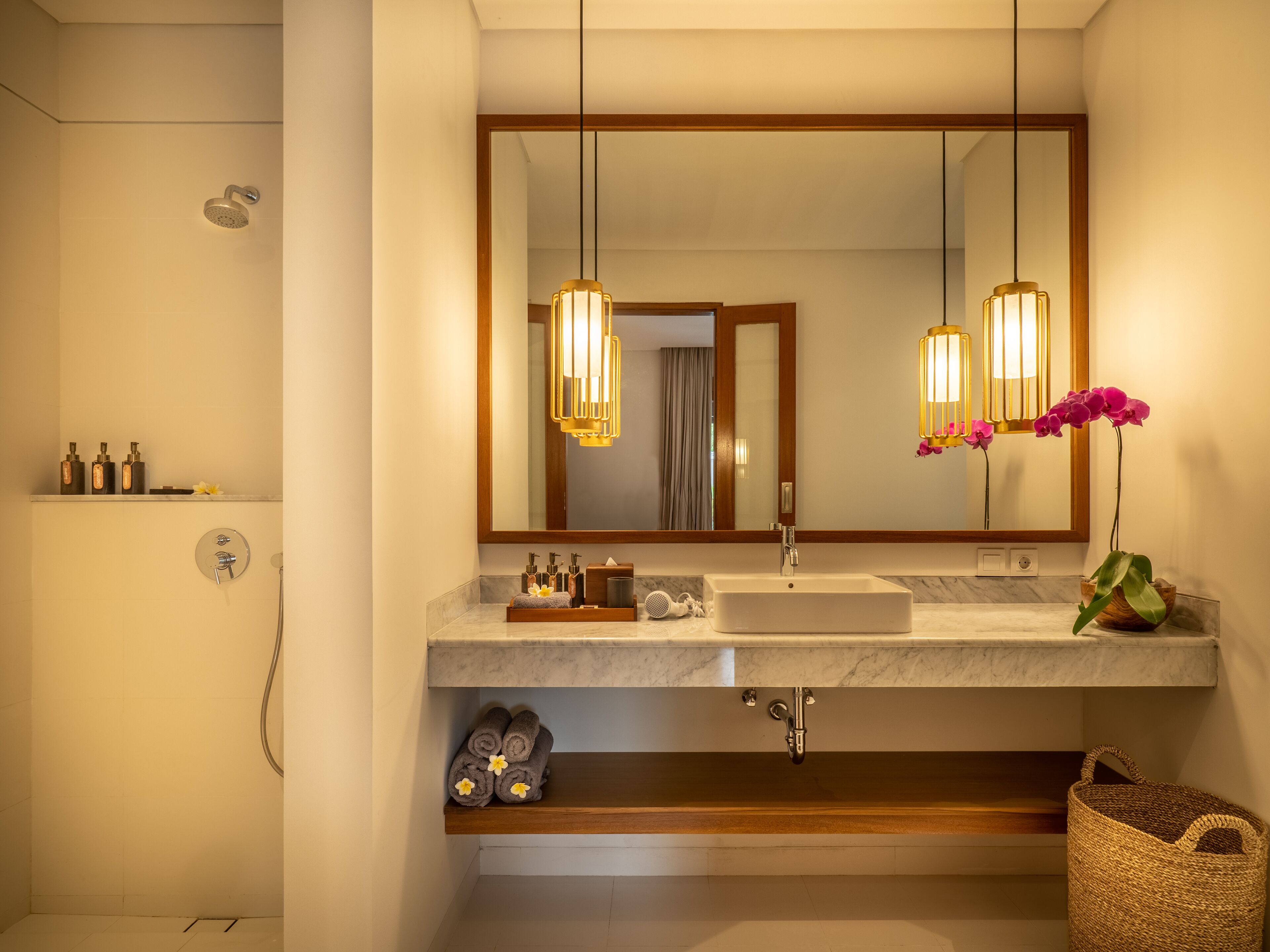 A modern bathroom with a large mirror, two pendant lights, a sink, and a shower.
