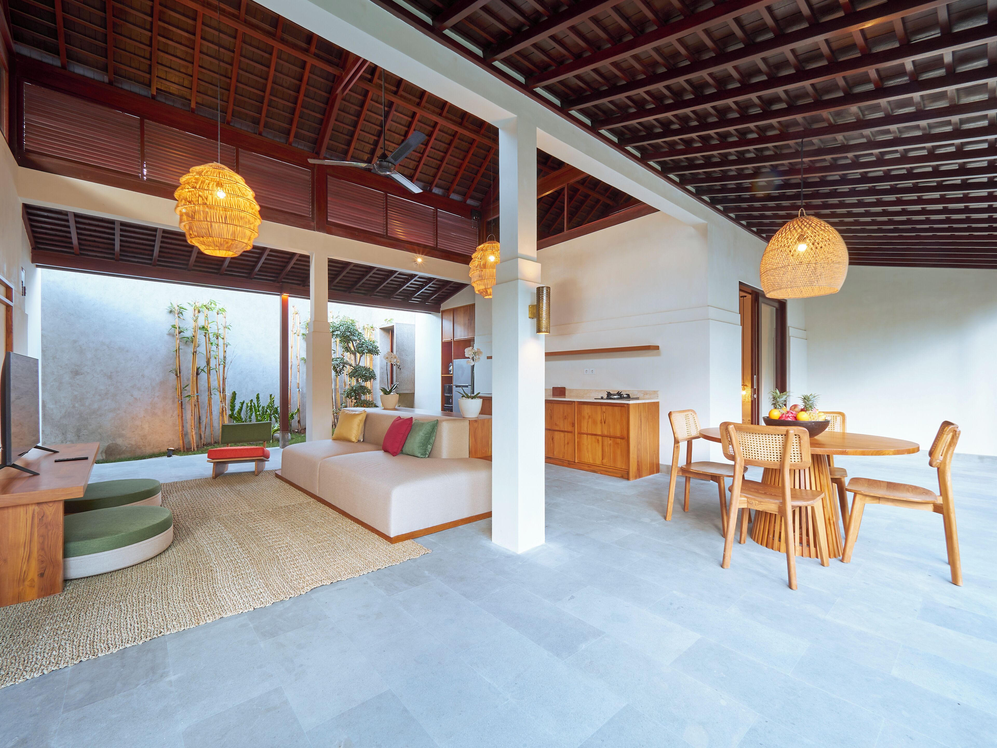 A spacious living area with a sofa, dining table, and chairs, a kitchen area, and large windows with a view of greenery.