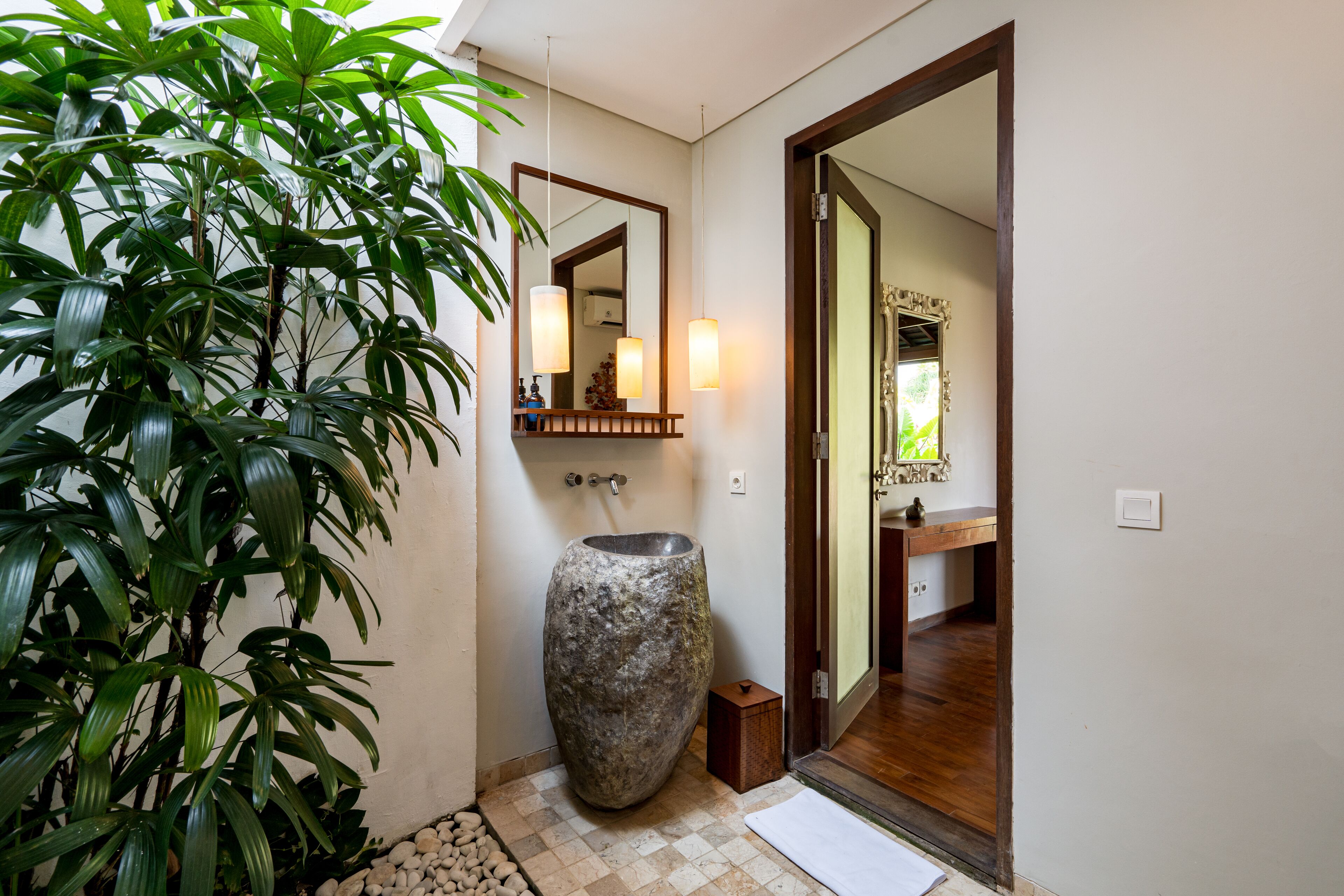 A bathroom with a large stone sink, a mirror, and a plant.