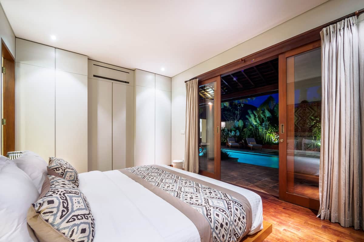 Un dormitorio con una cama grande y una puerta corrediza de vidrio que da a una zona de piscina.