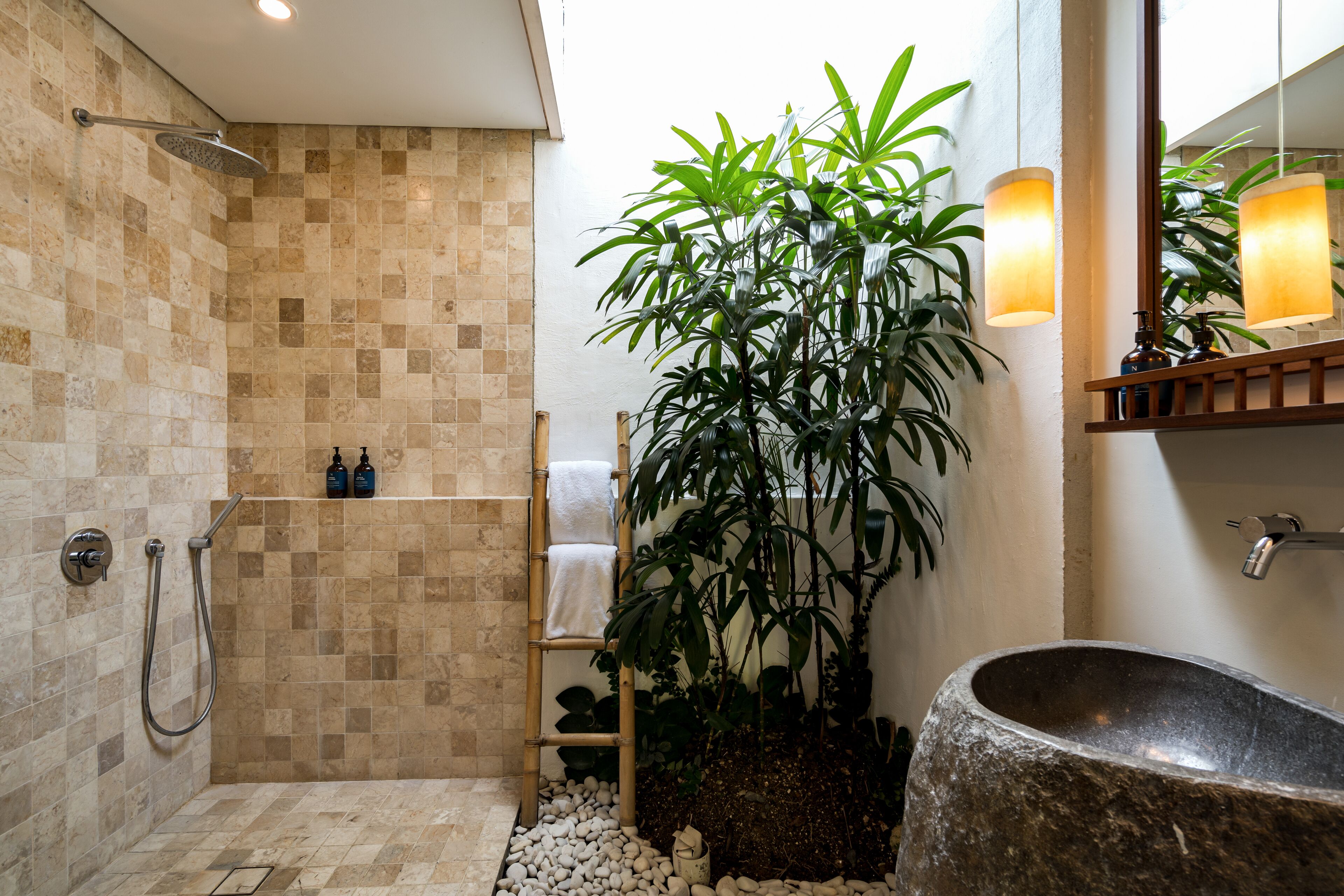 A modern bathroom with a stone sink, a shower with a rain showerhead, a bamboo ladder, and a large potted plant.
