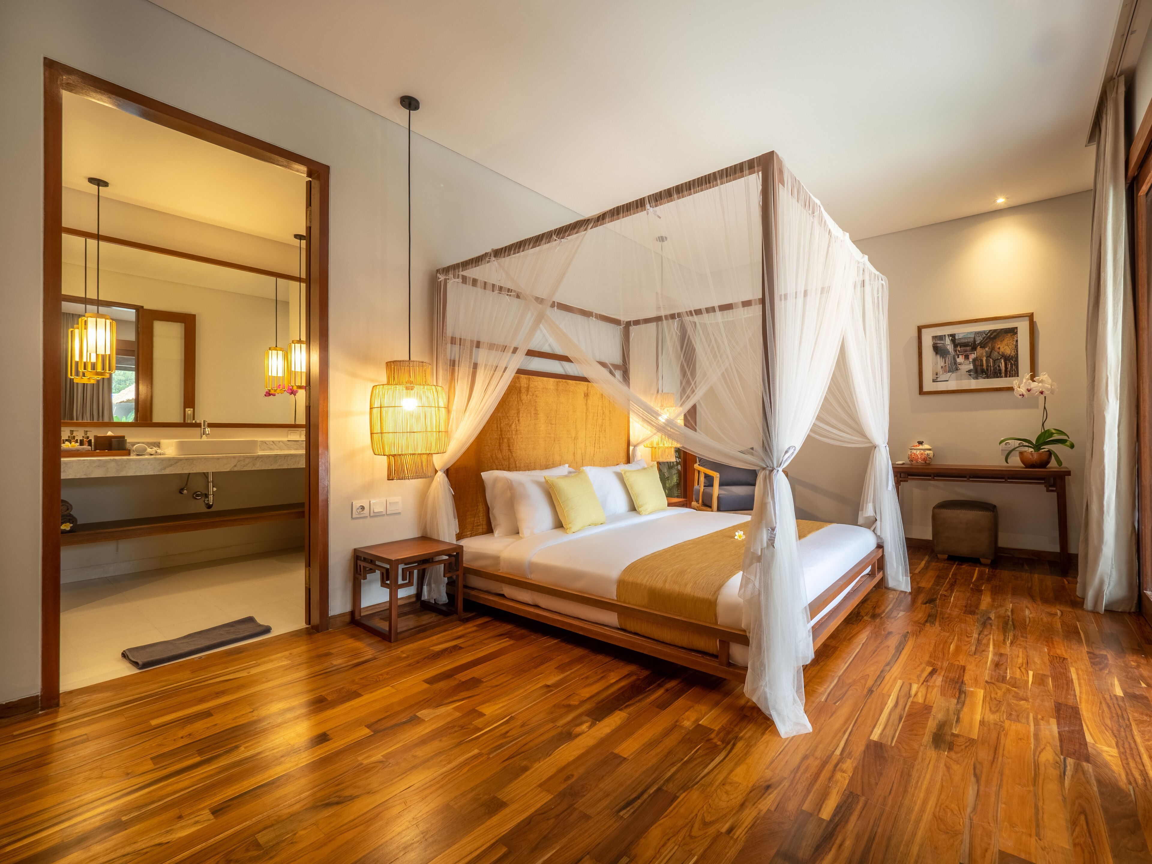 A spacious bedroom with a four-poster bed, a bedside table, a nightstand, a large mirror, and a console table with a vase of flowers.