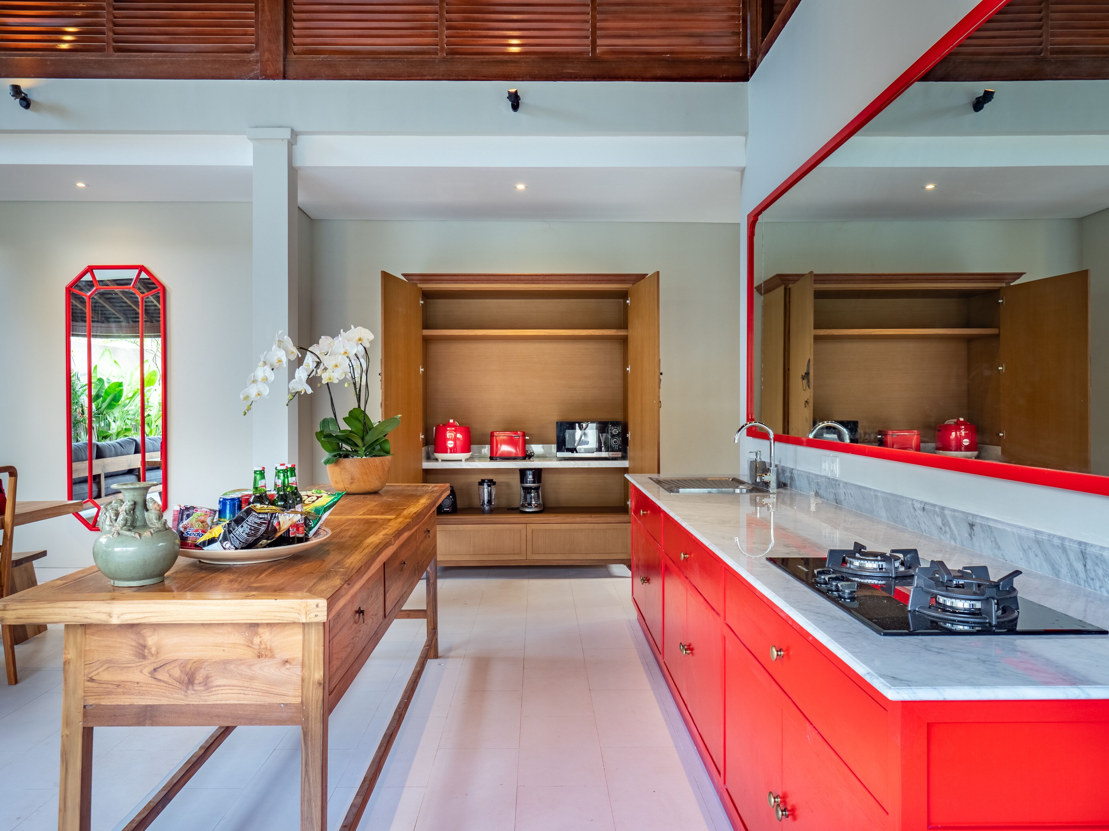 A modern kitchen with wooden cabinets, a red countertop, and a large mirror.