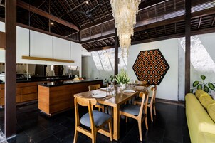 Una cocina moderna con una isla de madera, una zona de comedor con una mesa grande y sillas, y un sofá amarillo.