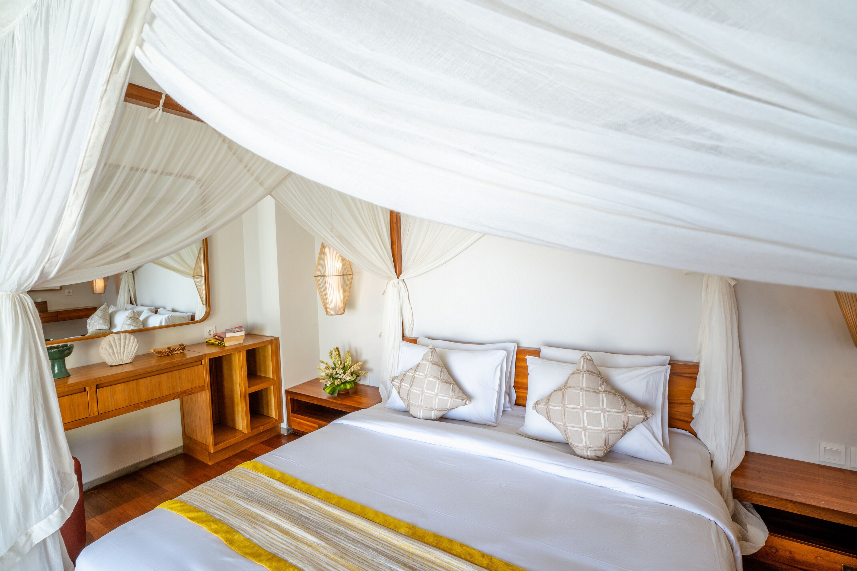 A bedroom with a canopy bed, wooden bedside tables, a mirror, and a small plant.