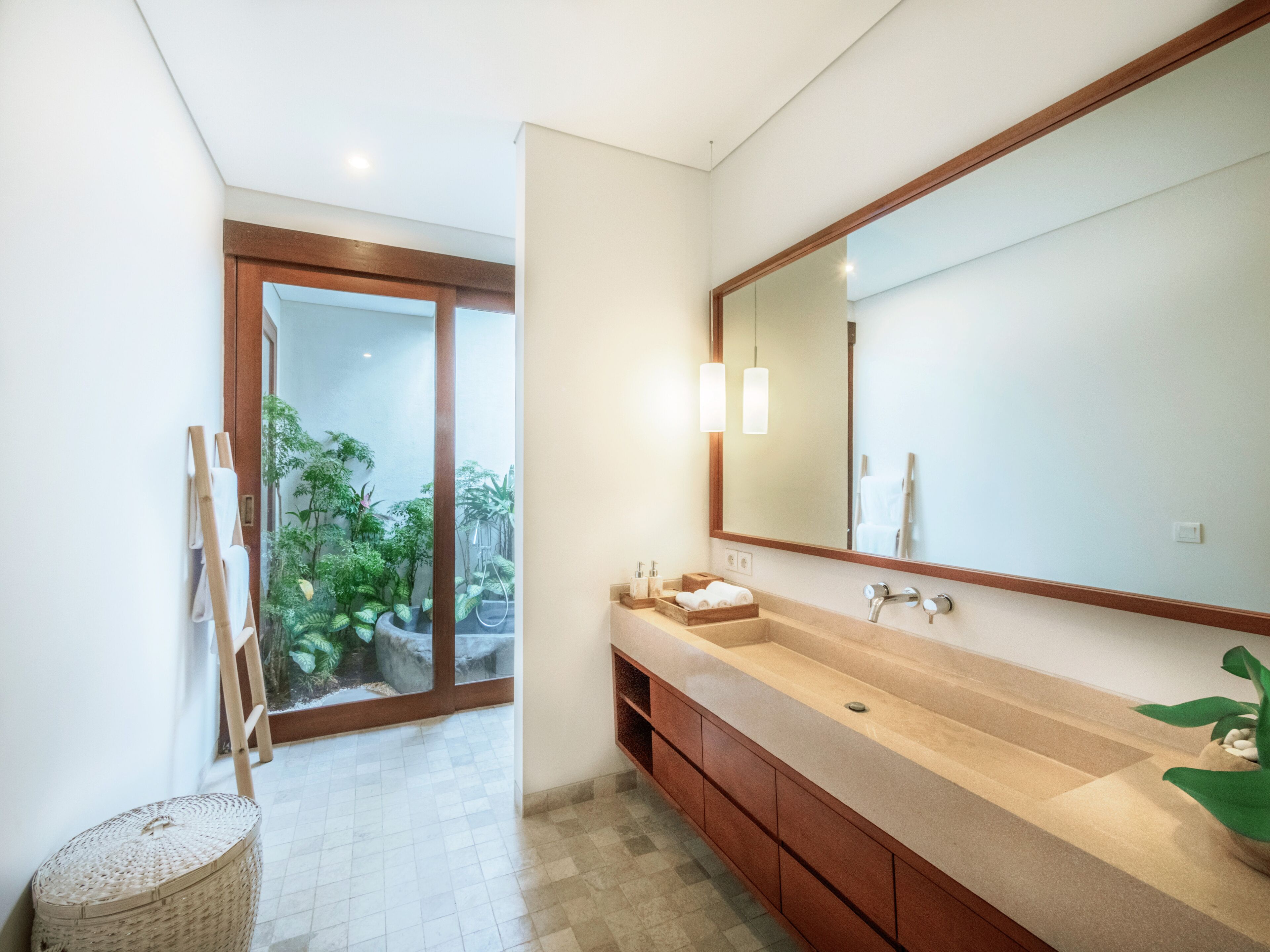 Un baño moderno con un espejo grande, armarios de madera y vistas a un jardín a través de una puerta de cristal.