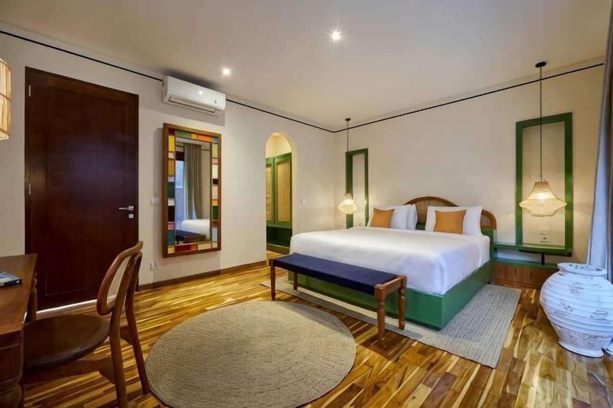 Un dormitorio con cama, escritorio, silla, espejo y ventana.