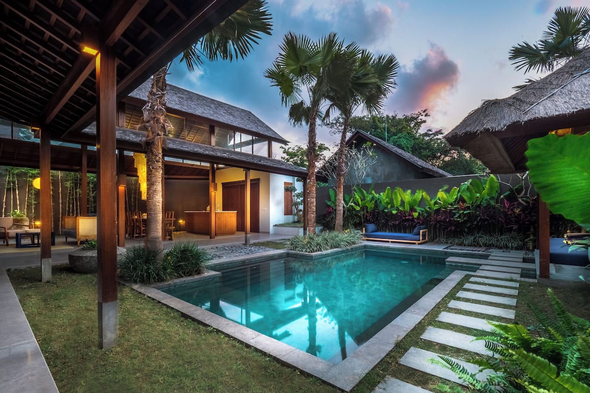 Un resort moderno con piscina, mobiliario de exterior y exuberante jardinería tropical.