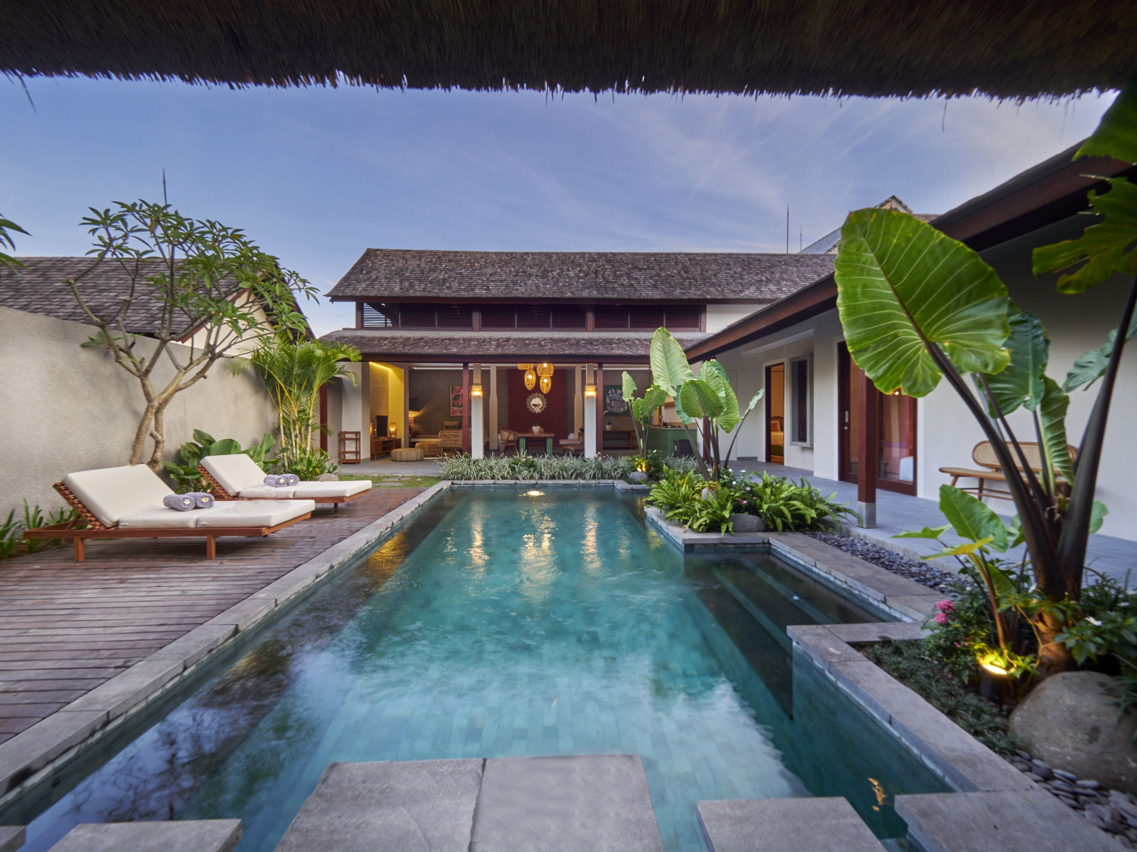 A poolside area with lounge chairs, a thatched roof, and tropical plants.