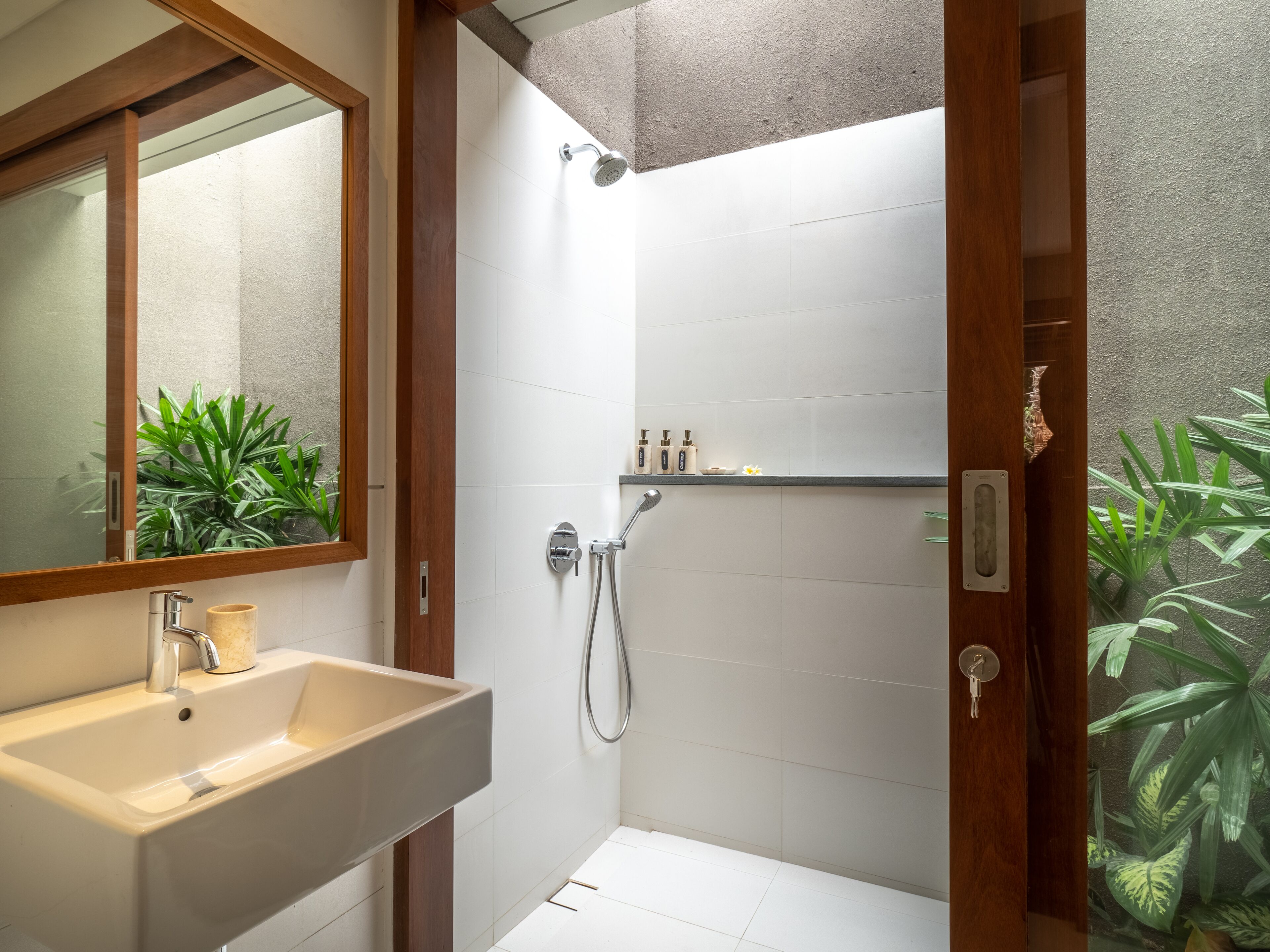 A modern bathroom with a sink, mirror, shower, and shelves with toiletries.