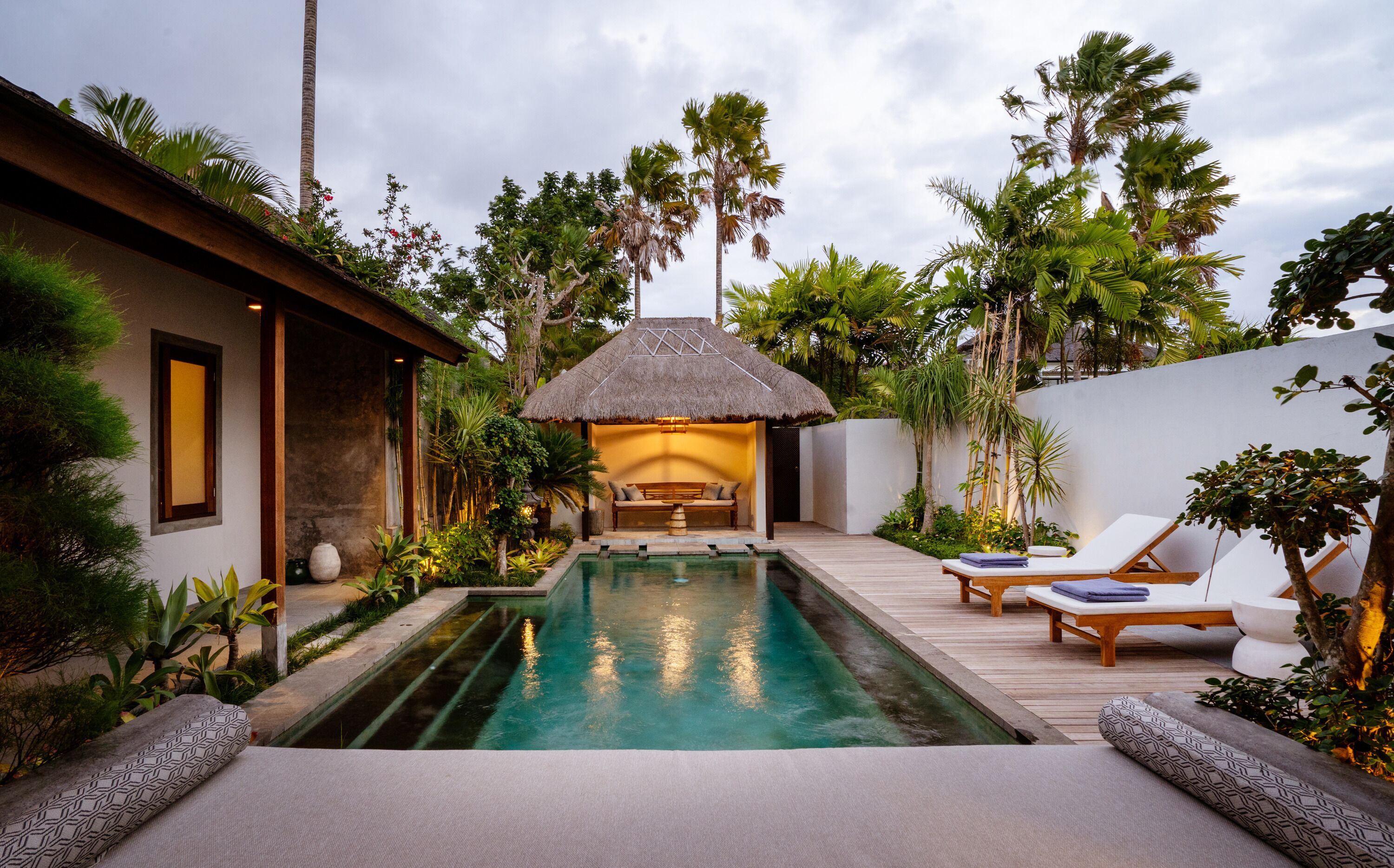 Un espace aménagé au bord de la piscine, avec une structure à toit de chaume, des chaises longues et une terrasse en bois.