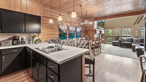 A modern kitchen with a large island, dark cabinets, and pendant lighting.