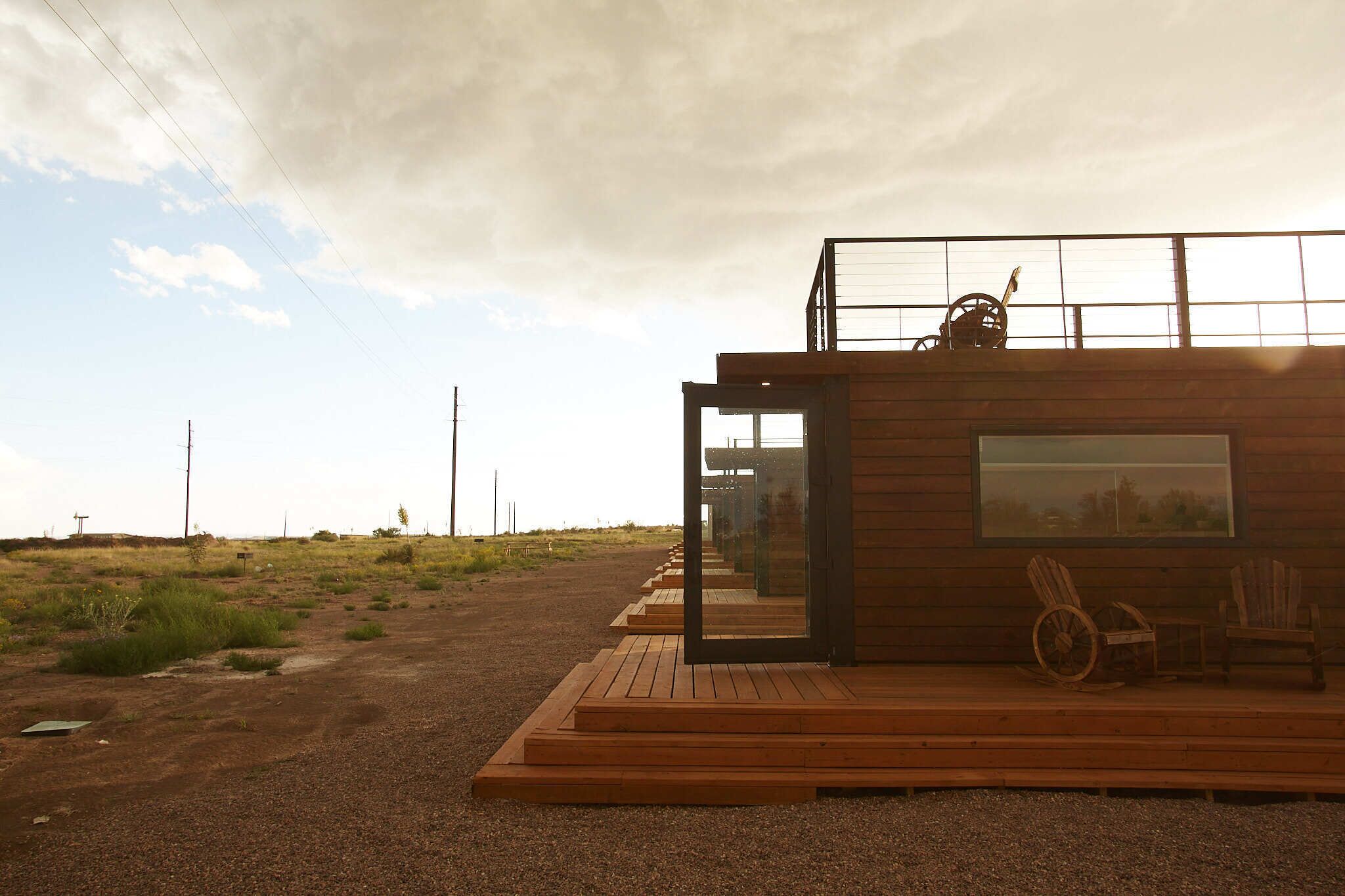 Een moderne houten cabin met een glazen deur, een rolstoel en een groot raam met uitzicht op een grasveld.