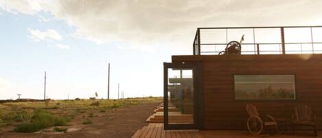 Een moderne houten cabin met een glazen deur, een rolstoel en een groot raam met uitzicht op een grasveld.