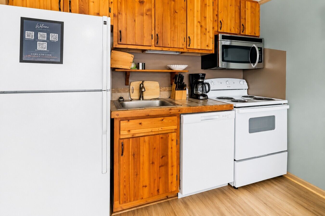 A kitchen with wooden cabinets, a white refrigerator, a microwave, a stove, and a dishwasher.