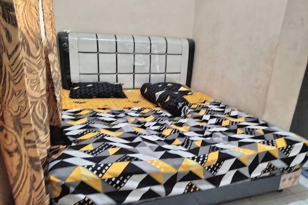 A bed with a patterned bedspread, a headboard with a grid design, and a plain wall.