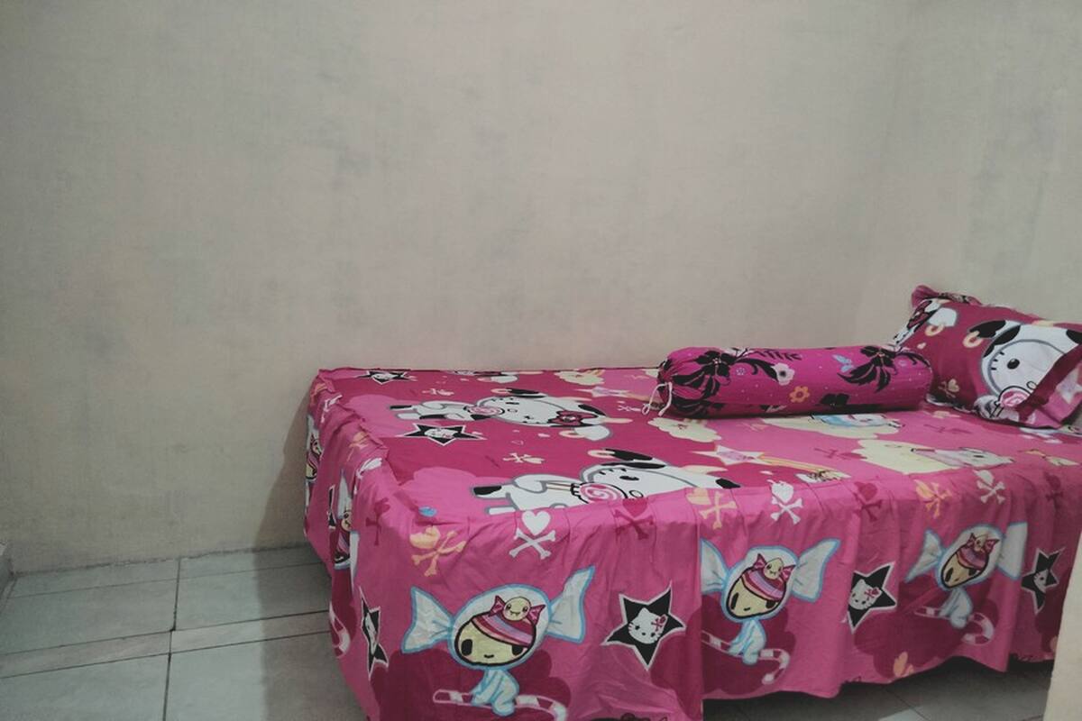 A small, single-bed room with a pink bedspread featuring cartoon characters and a Hello Kitty design.