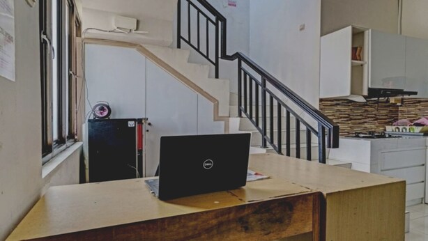 A compact kitchen with a gas stove, a refrigerator, and a wooden dining table with a laptop. - Hotel O Nany Ayahanda Syariah (Medan)