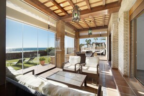 Un balcon spacieux offrant une vue sur la mer, des meubles en osier et une porte vitrée donnant sur un espace extérieur aménagé pour s’asseoir.