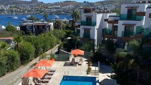 Área de piscina en la azotea con sillones de descanso y sombrillas, con vistas a un puerto deportivo y edificios residenciales.