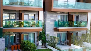 Un moderno edificio de apartamentos con balcones de vidrio, mobiliario exterior y un pequeño jardín.