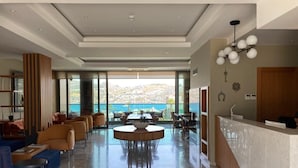 Un vestíbulo amplio con una mesa redonda central, zona de estar con sofás y sillones, un mostrador de recepción y grandes ventanales con vistas al mar.