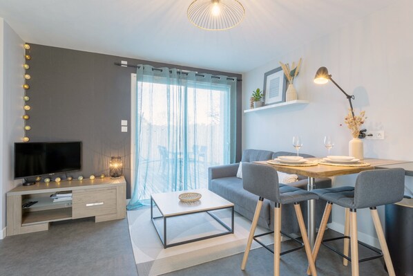 Un salon moderne doté d’un téléviseur à écran plat, d’une table basse, d’un canapé et d’un coin repas avec des chaises et une table.
