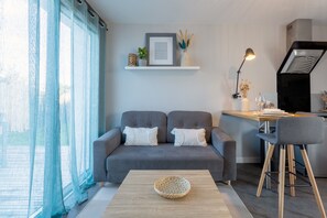 Un salon moderne avec un canapé gris, une table basse en bois et un coin cuisine doté d’un tabouret de bar.