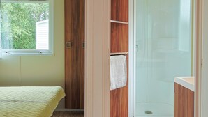 A bedroom with a bed, a window, a wooden wardrobe, and a shower area. - Mobile Home "Le Marie Elodie 85" with 2 Shared Pools, Private Terrace & Wi-Fi (Angles)