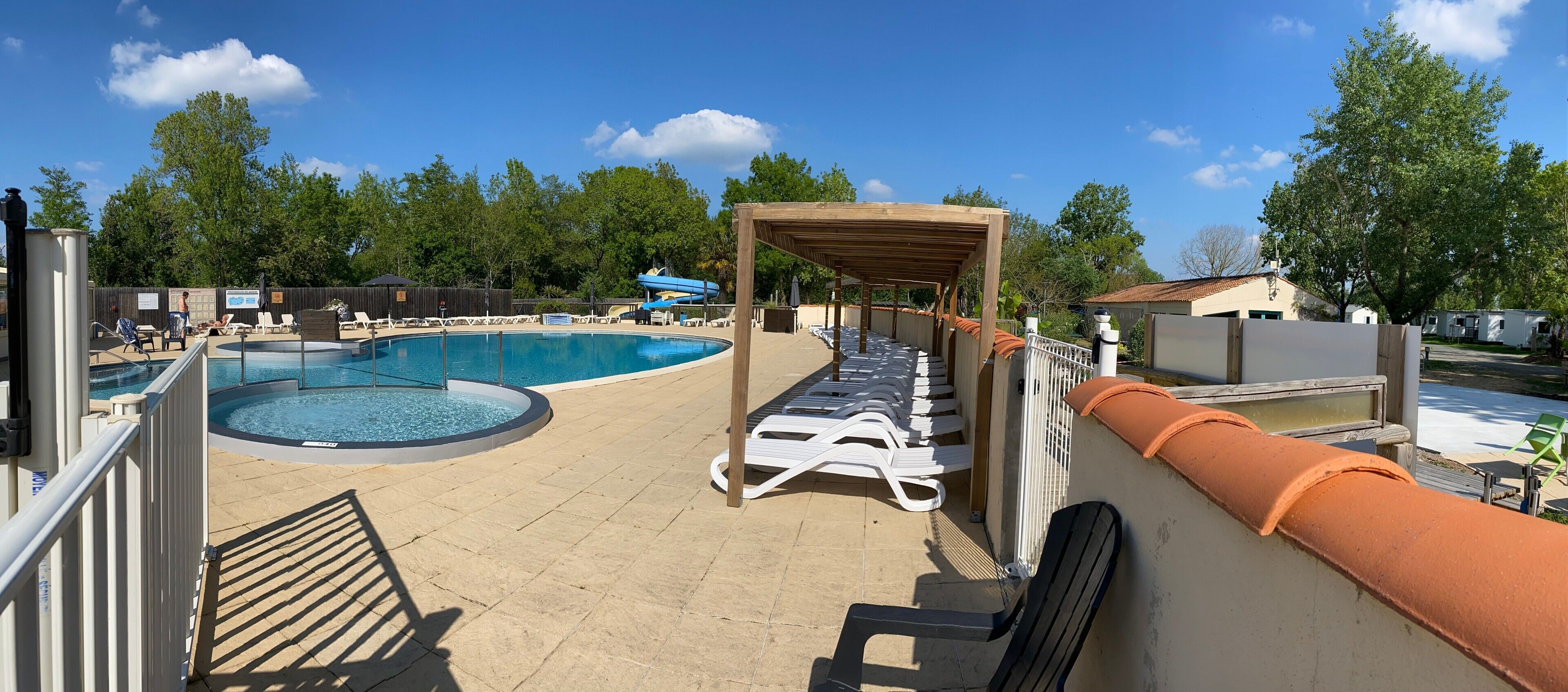 Ein Pool mit Liegestühlen, einer überdachten Sitzgruppe und einer umzäunten Holzterrasse.