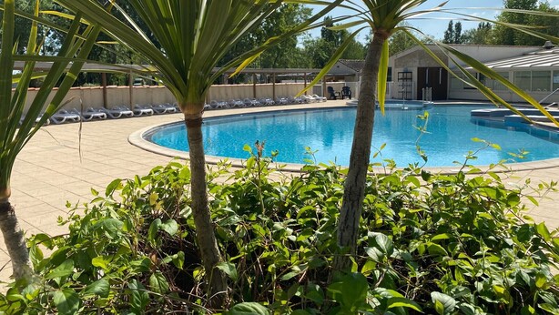 A swimming pool surrounded by lush greenery and a building in the background. - Mobile Home "Le Marie Elodie 85" with 2 Shared Pools, Private Terrace & Wi-Fi (Angles)
