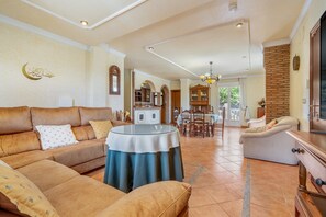 A spacious living room with a sofa, a round table, and a dining area with chairs and a cabinet.