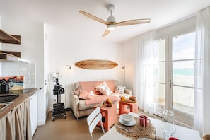 A modern living room with a sofa, coffee table, and dining table, a ceiling fan, and a view of the sea. - Studio Les Pins with Sea View, Private Terrace, and Wi-Fi (RIVEDOUX PLAGE)