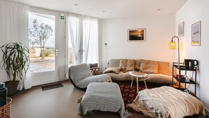 Un salon moderne comprenant un canapé, un fauteuil et un pouf, une petite table d’appoint et une lampe.
