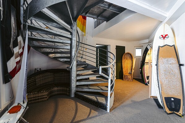 A spiral staircase with a flag, a surfboard, and a woven bench.