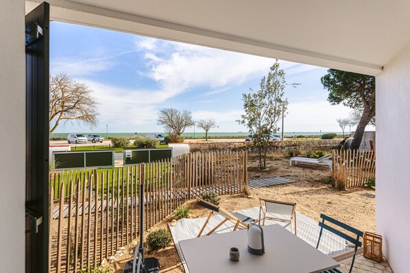 A patio with a table and chairs, a view of the beach, and a fence.
